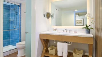 A bathroom with a glass-enclosed shower, a white toilet, a wooden vanity with a mirror, and a potted orchid.