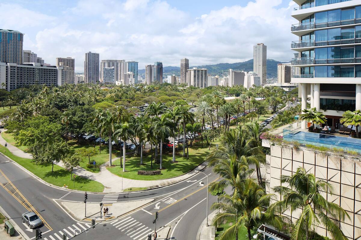 A cityscape with tall buildings, a road intersection, and a hotel with a pool and outdoor seating.