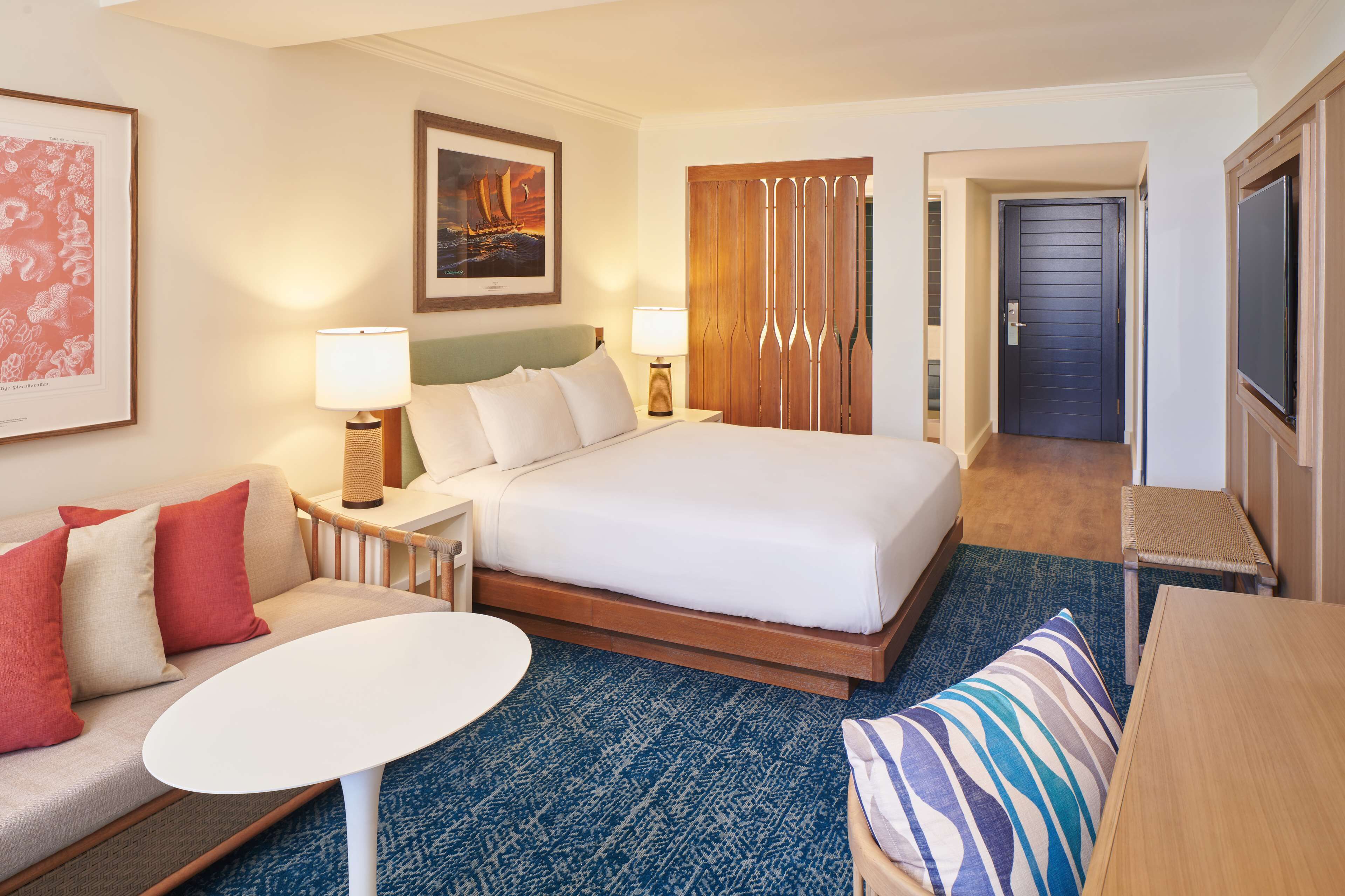 Een hotelkamer met een bed, een bank, een kleine tafel, een lamp, een televisie en een deur.
