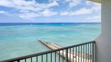 A balcony with a view of the ocean, a pier, and a sandy beach.
