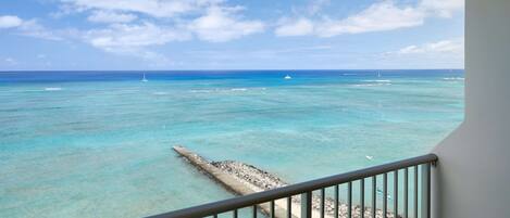 A balcony with a view of the ocean, a pier, and a sandy beach.