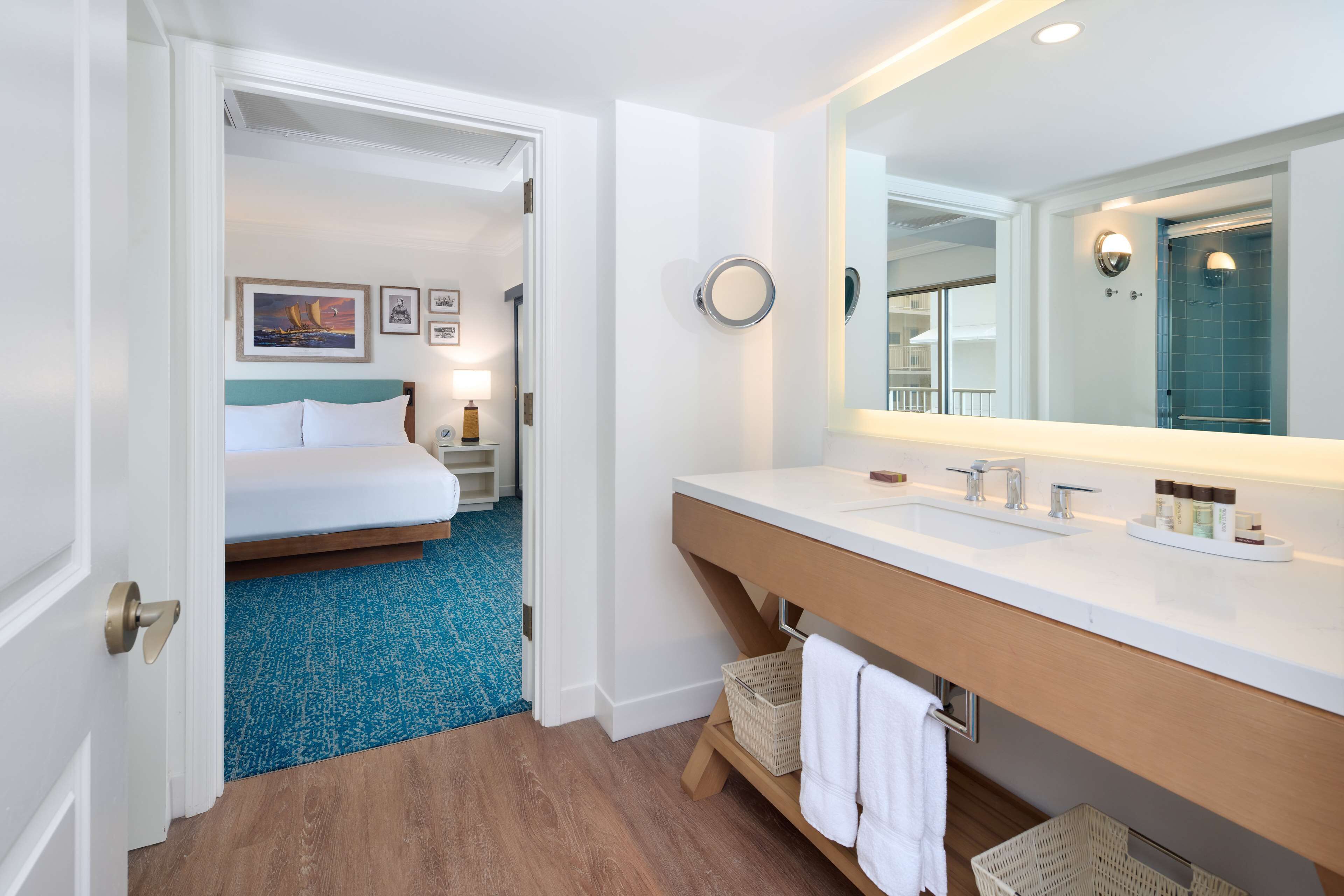 A hotel room with a bed, a bathroom with a large mirror, and a blue carpet.