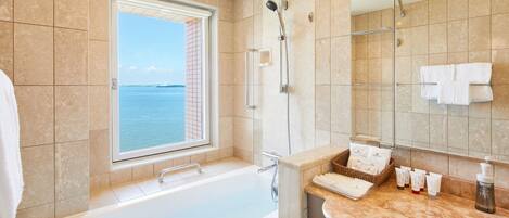 A modern bathroom with a bathtub, a shower, and a large window offering a view of the sea.