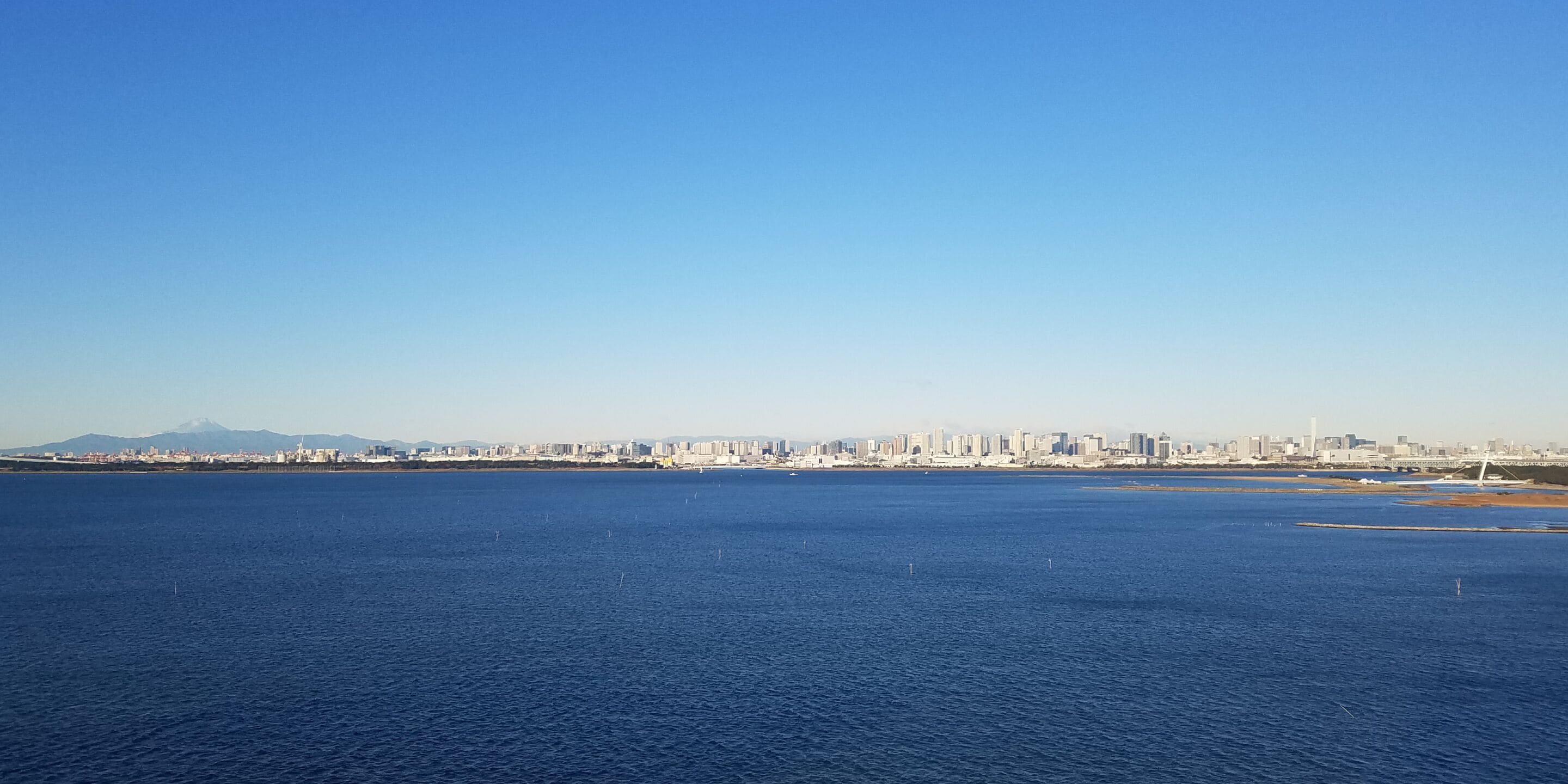 A coastal cityscape with a large body of water in the foreground and a skyline of buildings in the background.