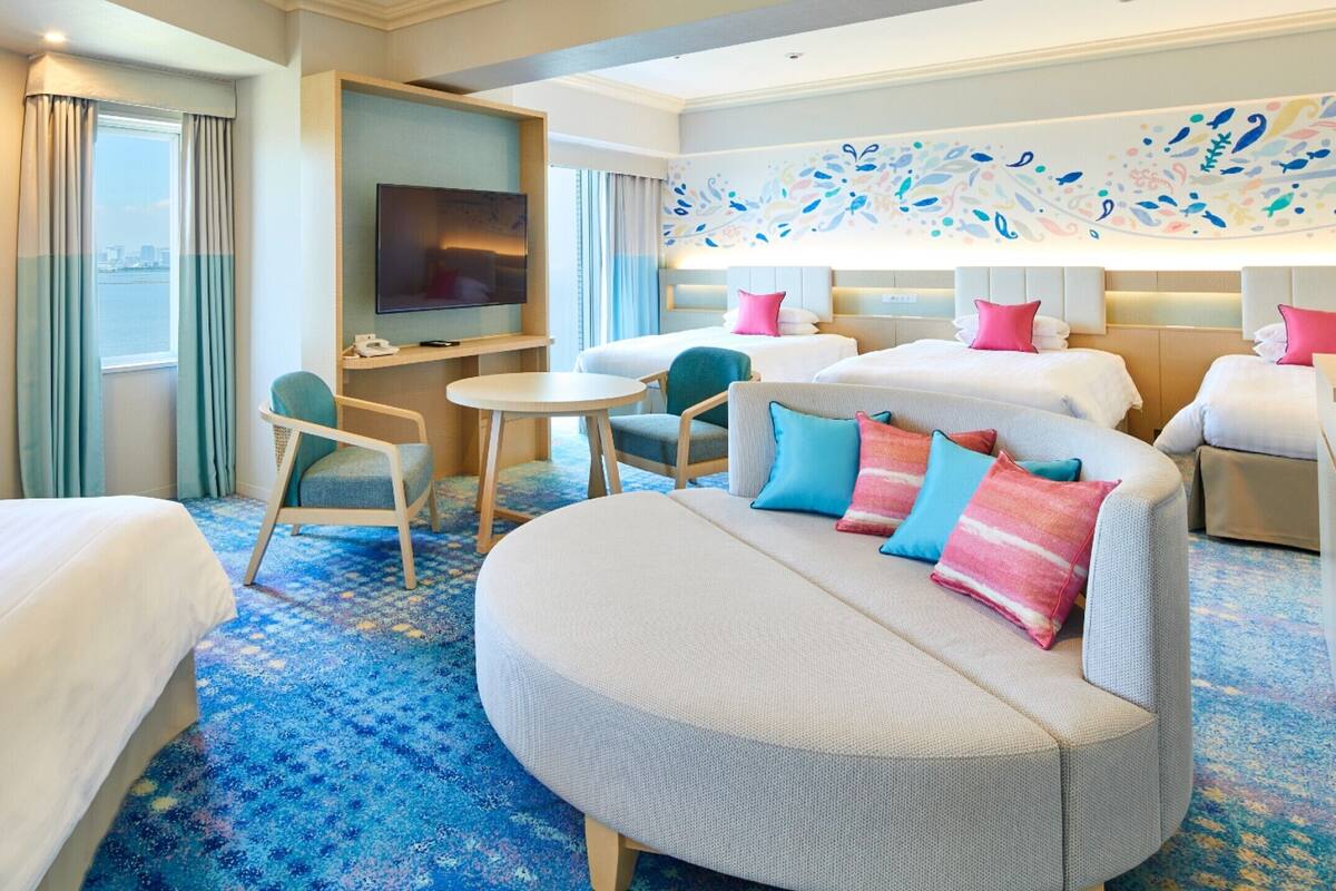 Ein Hotelzimmer mit zwei Betten, einem Sofa, einem Fernseher, einem Schreibtisch und einem Sessel.