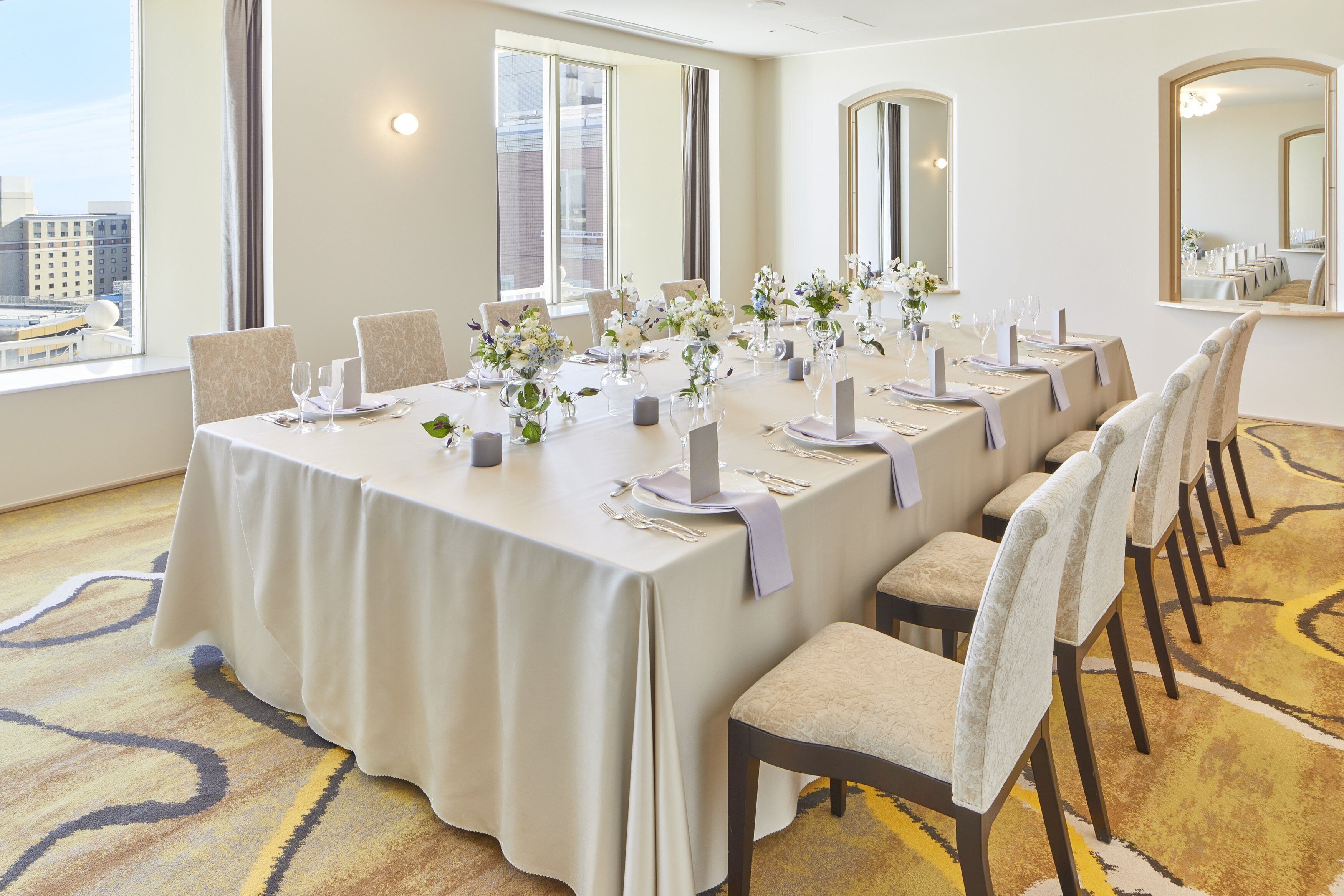 A conference room with a long table set for a meeting, large windows, and a carpeted floor.