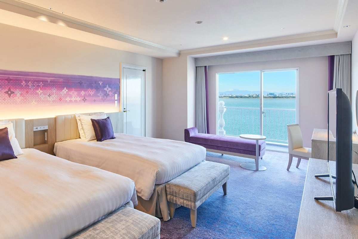 Ein Hotelzimmer mit zwei Betten, einem Fernseher, einem kleinen Tisch und Blick auf das Wasser.