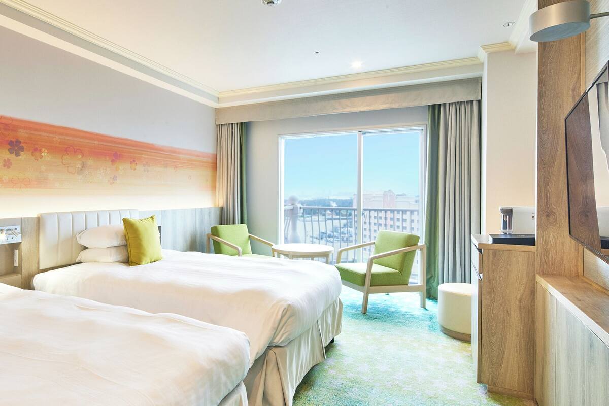 Ein Hotelzimmer mit zwei Betten, einem Fernseher, einem kleinen Tisch und einem Sessel.