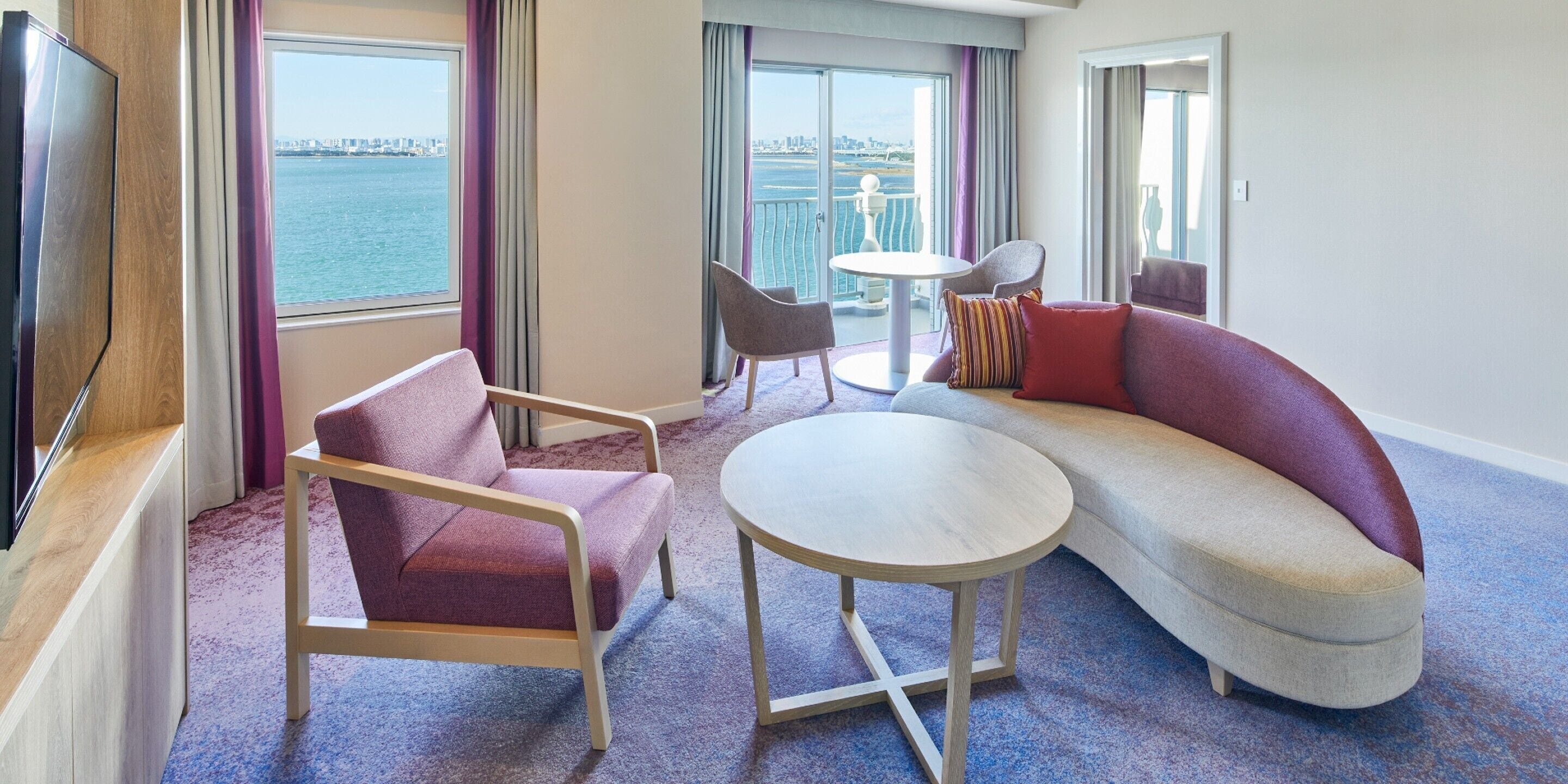 A modern hotel room with a sofa, armchair, round table, and a TV.