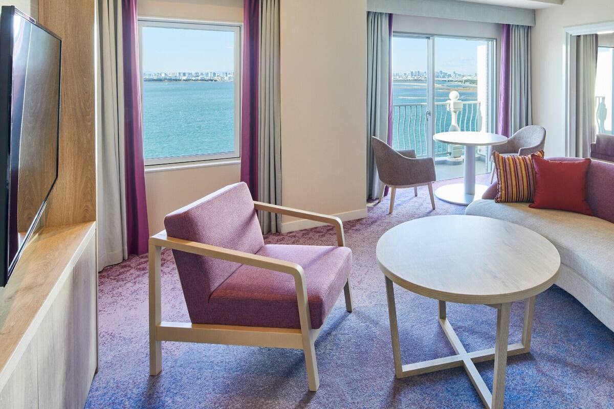 Ein modernes Hotelzimmer mit Sofa, Sessel, rundem Tisch und Fernseher.