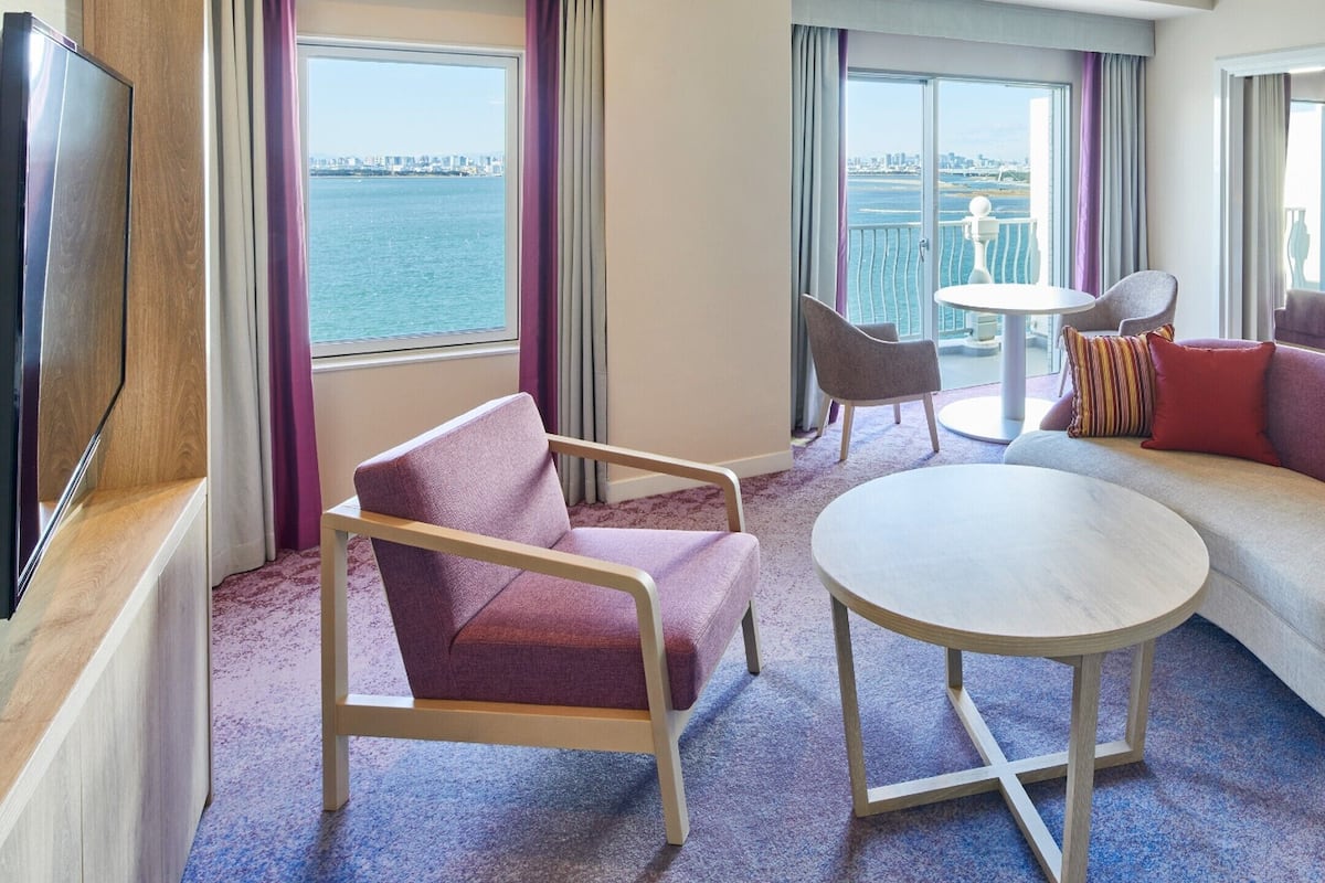 Une chambre d’hôtel moderne équipée d’un canapé, d’un fauteuil, d’une table ronde et d’un téléviseur.