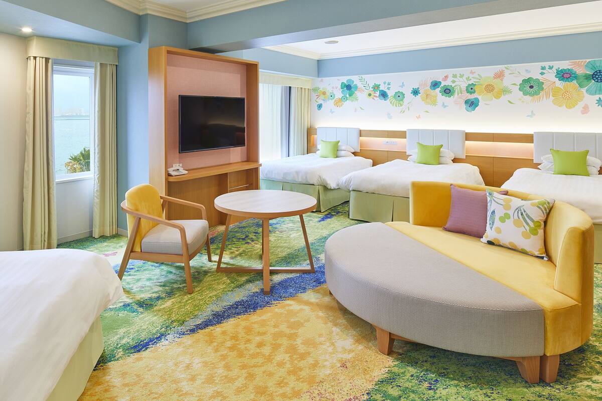 Ein Hotelzimmer mit zwei Betten, einem Sofa, einem Sessel, einem Fernseher und einem Fenster mit Vorhängen.