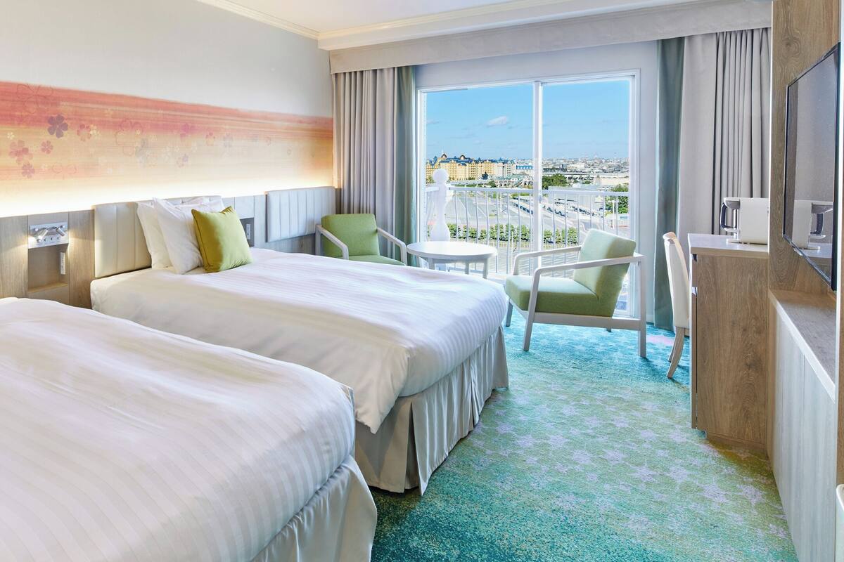 Ein Hotelzimmer mit zwei Betten, einem Balkon mit Stadtblick und einem kleinen Tisch.