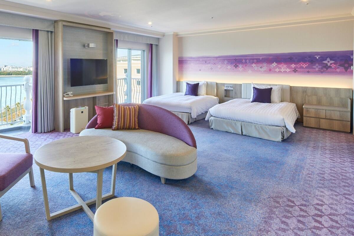 Ein Hotelzimmer mit einer Couch, einem Sessel, einem runden Tisch und zwei Betten.