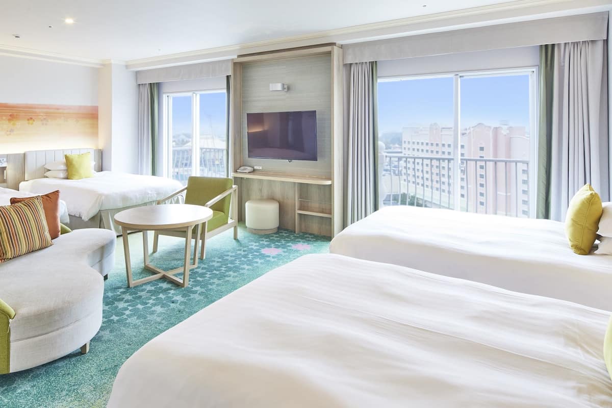 Ein Hotelzimmer mit zwei Betten, einem Fernseher, einem kleinen Tisch und Blick auf die Stadt.