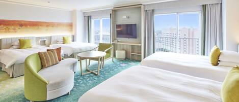 Ein Hotelzimmer mit zwei Betten, einem Fernseher, einem kleinen Tisch und Blick auf die Stadt.