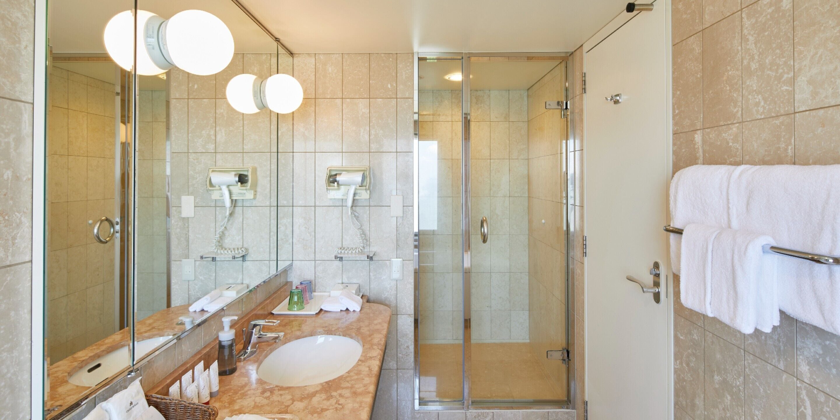 A modern bathroom with a glass-enclosed shower, a large mirror, and a marble countertop.