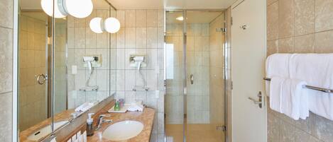 A modern bathroom with a glass-enclosed shower, a large mirror, and a marble countertop.