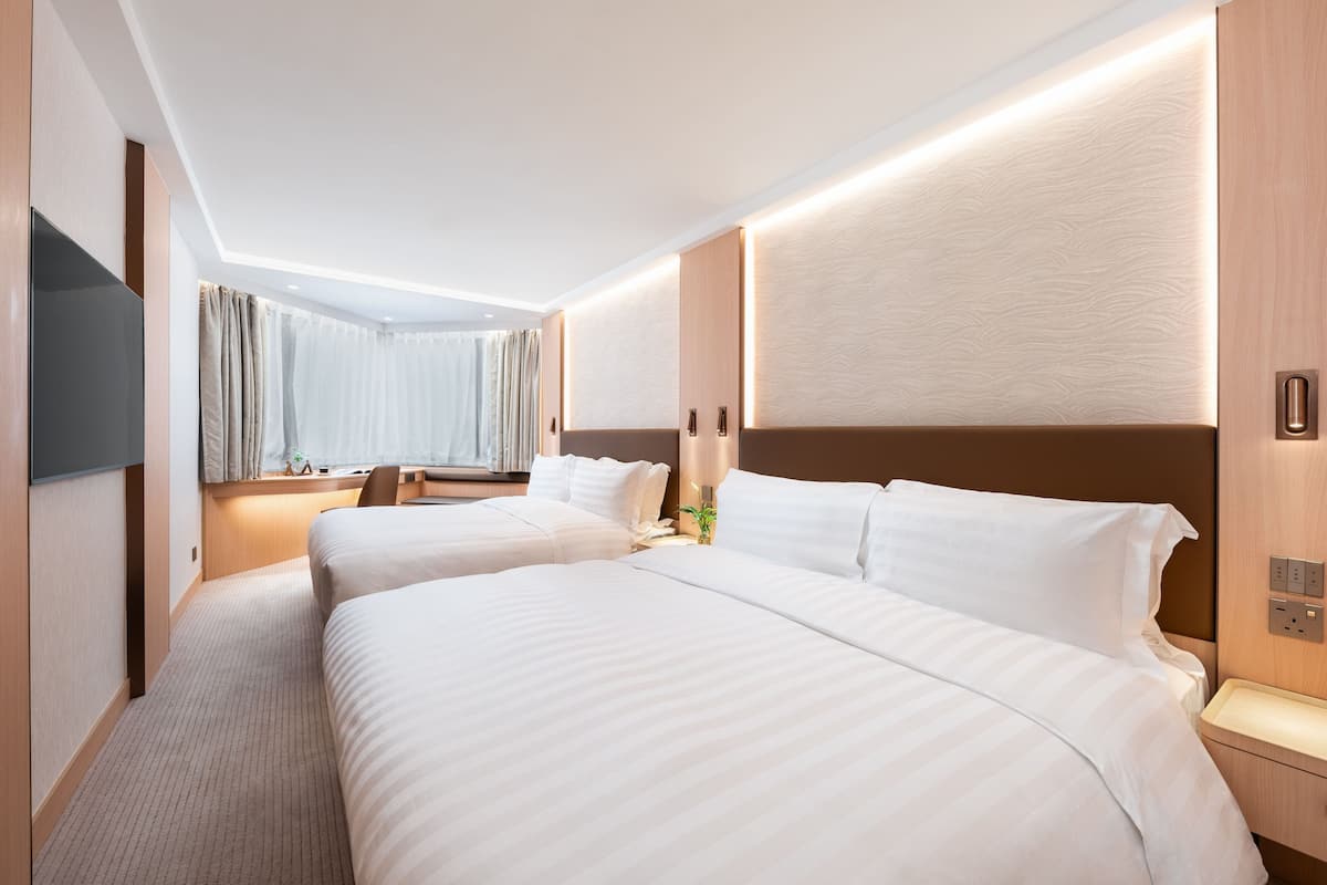 A hotel room with two beds, a flat-screen TV, a desk with a chair, and a window with curtains.