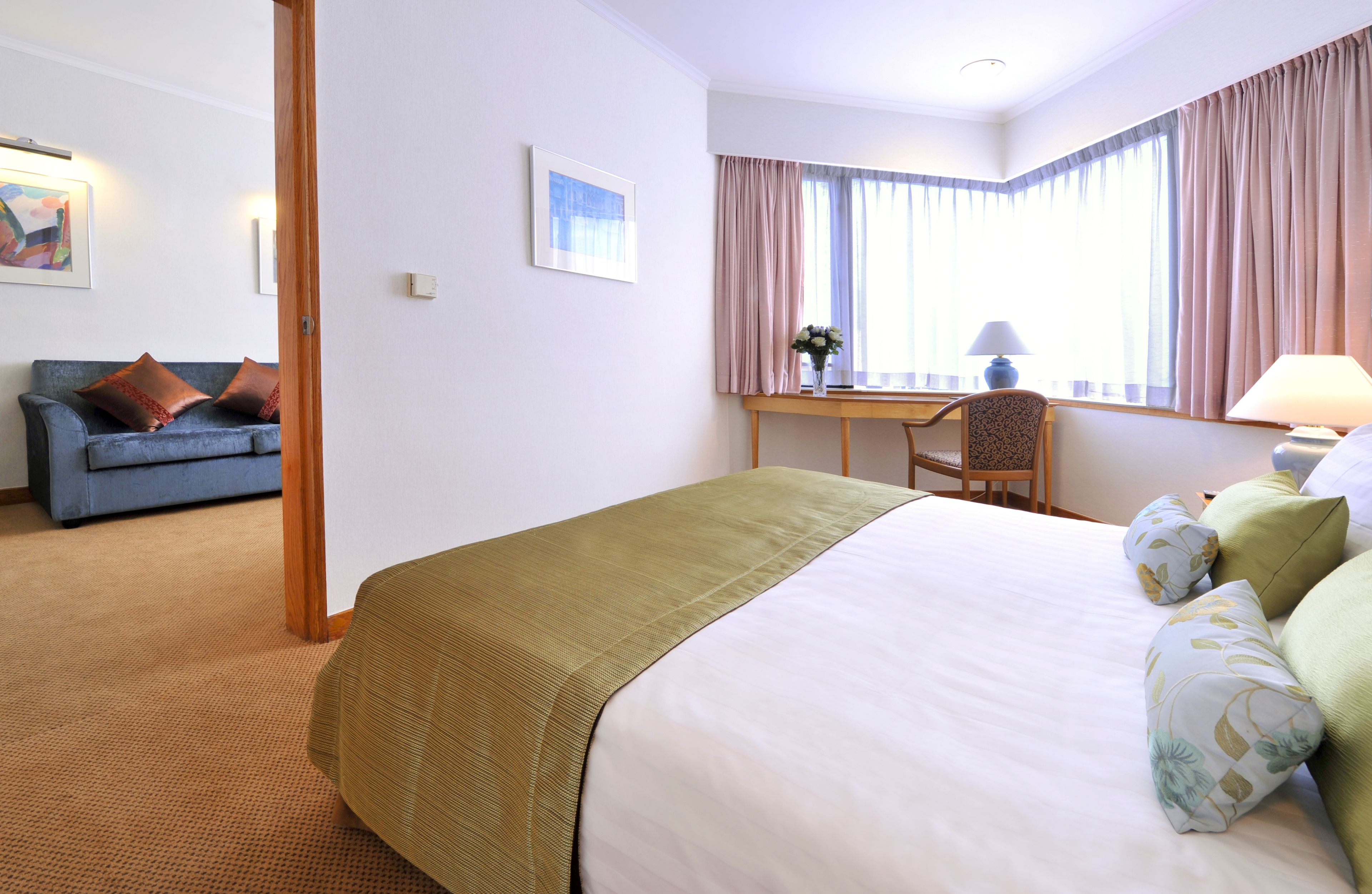 A hotel room with a large bed, a desk with a chair, a sofa, and a window with curtains.
