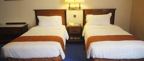 A hotel room with two single beds, a nightstand, a lamp, and a painting on the wall.