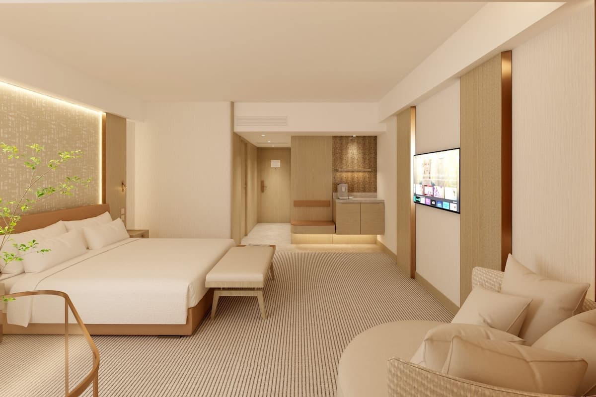 A modern hotel room with a large bed, a seating area, a TV, and a kitchenette.