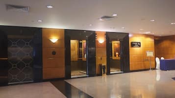 A hotel lobby with a reception desk, elevators, and a sign indicating the name of the hotel.