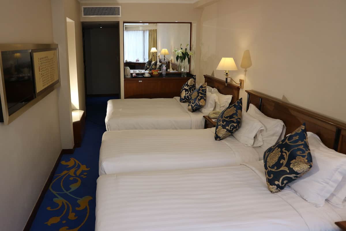 A hotel room with three beds, a desk, and a mirror.