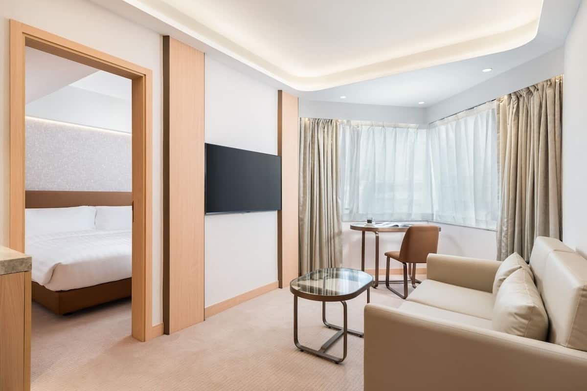 A hotel room with a bed, a sofa, a glass table, and a TV.