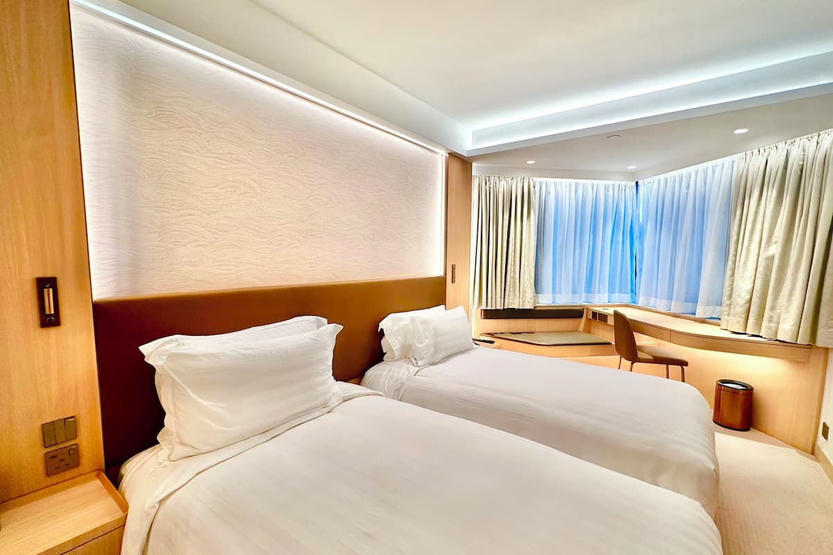 A hotel room with two beds, a desk, a chair, and a window with curtains.