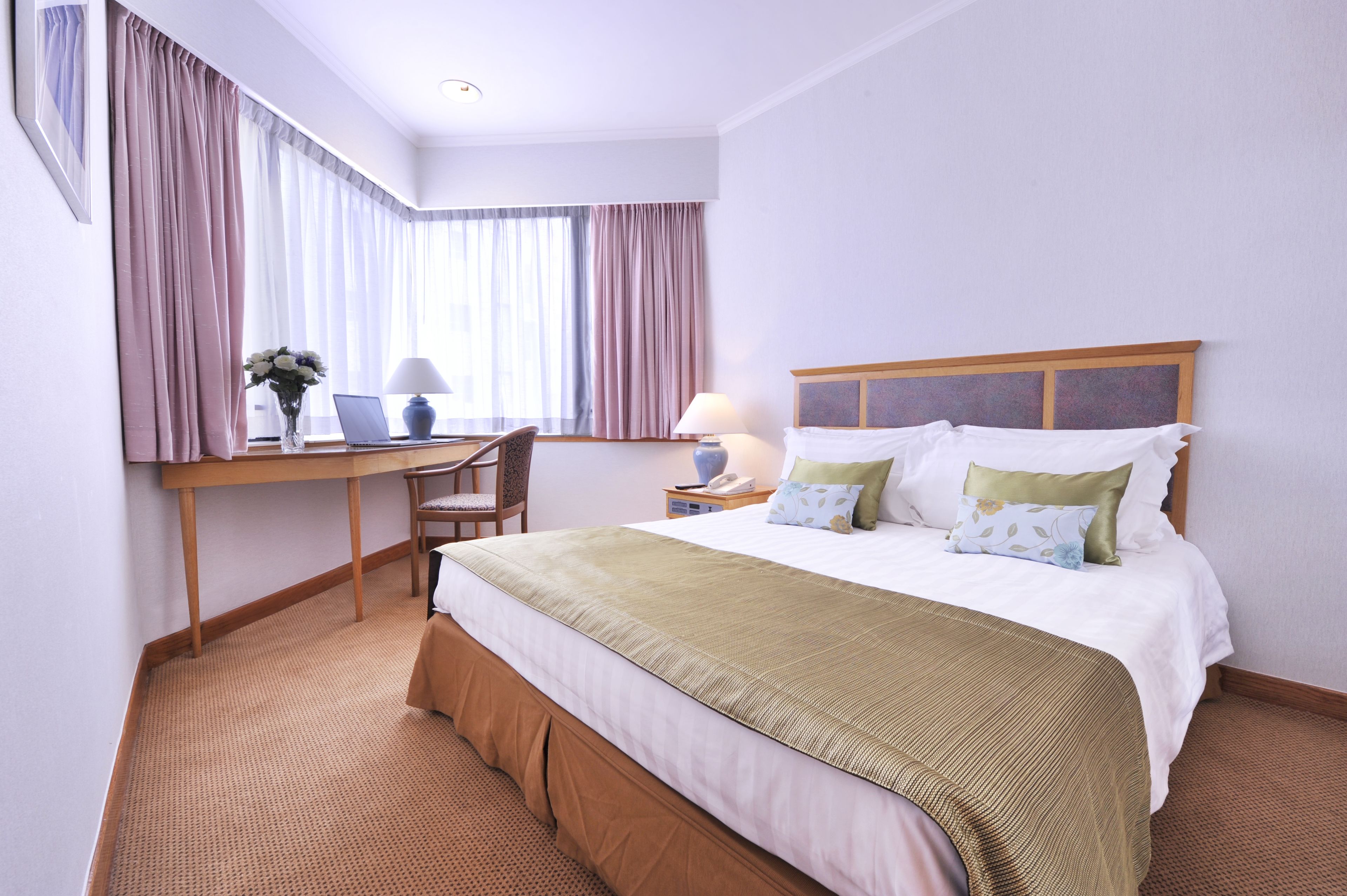 A hotel room with a bed, a desk with a chair, a lamp, and a window with curtains.