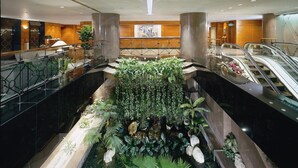 A modern hotel lobby with a central indoor garden, multiple floors, and an adjacent escalator. - The Kimberley Hotel (Kowloon)