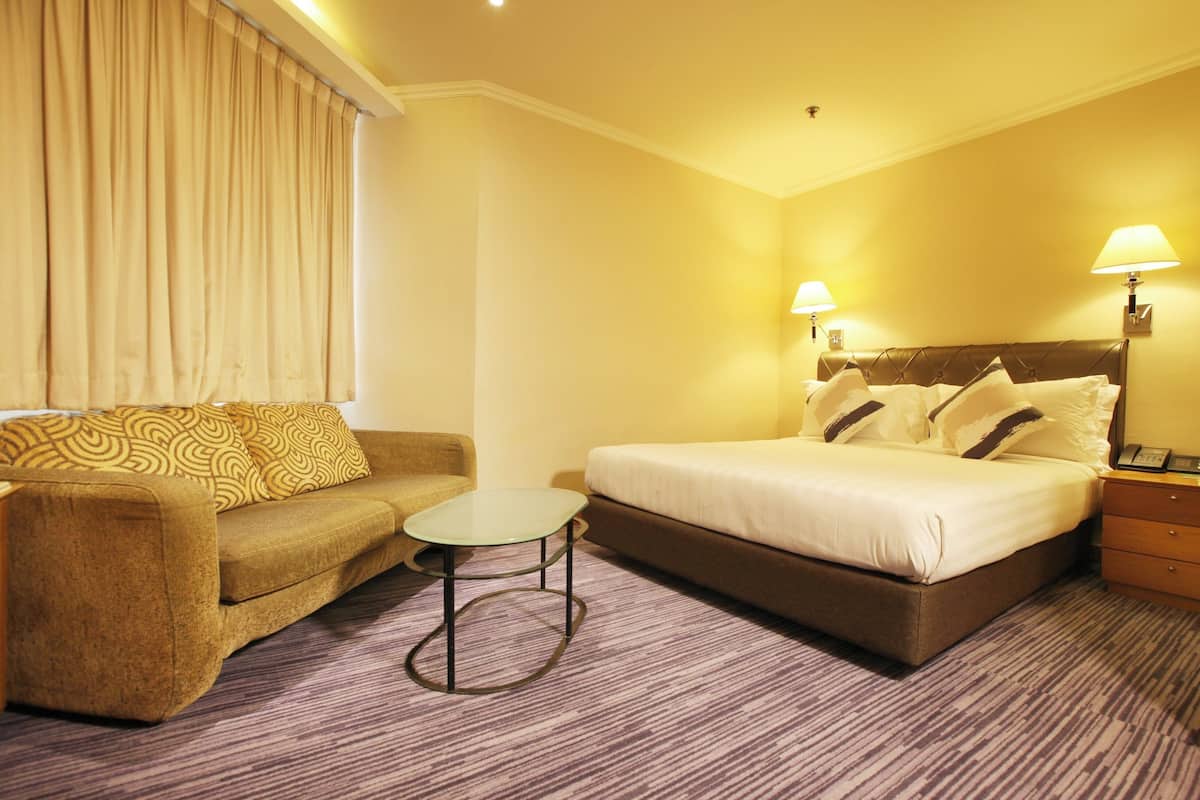 A hotel room with a bed, a sofa, a small table, and two bedside lamps.