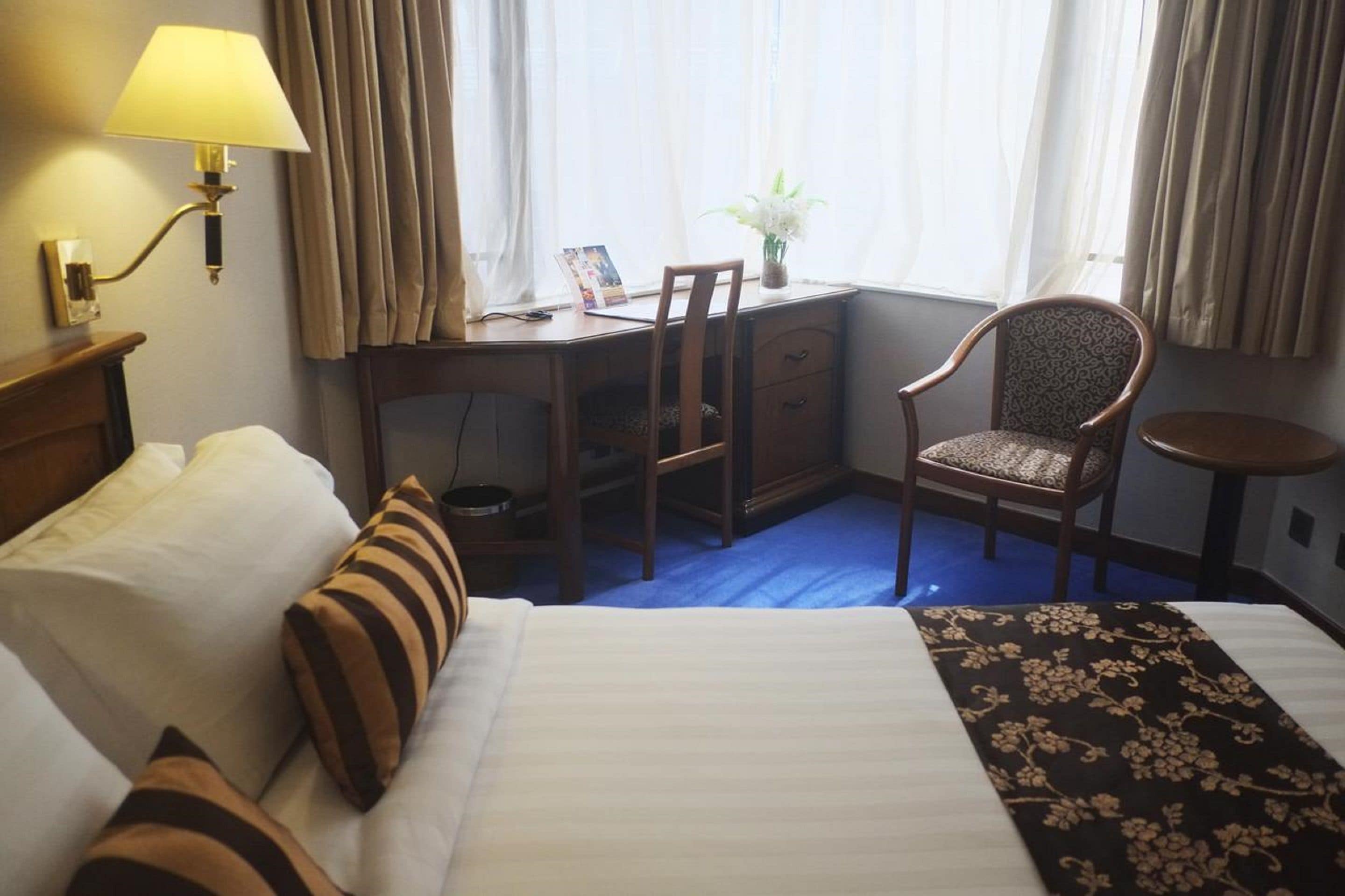 Een hotelkamer met een bed, bureau, stoel, lamp en raam met gordijnen.