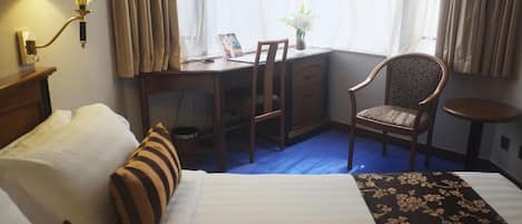 A hotel room with a bed, a desk, a chair, a lamp, and a window with curtains.