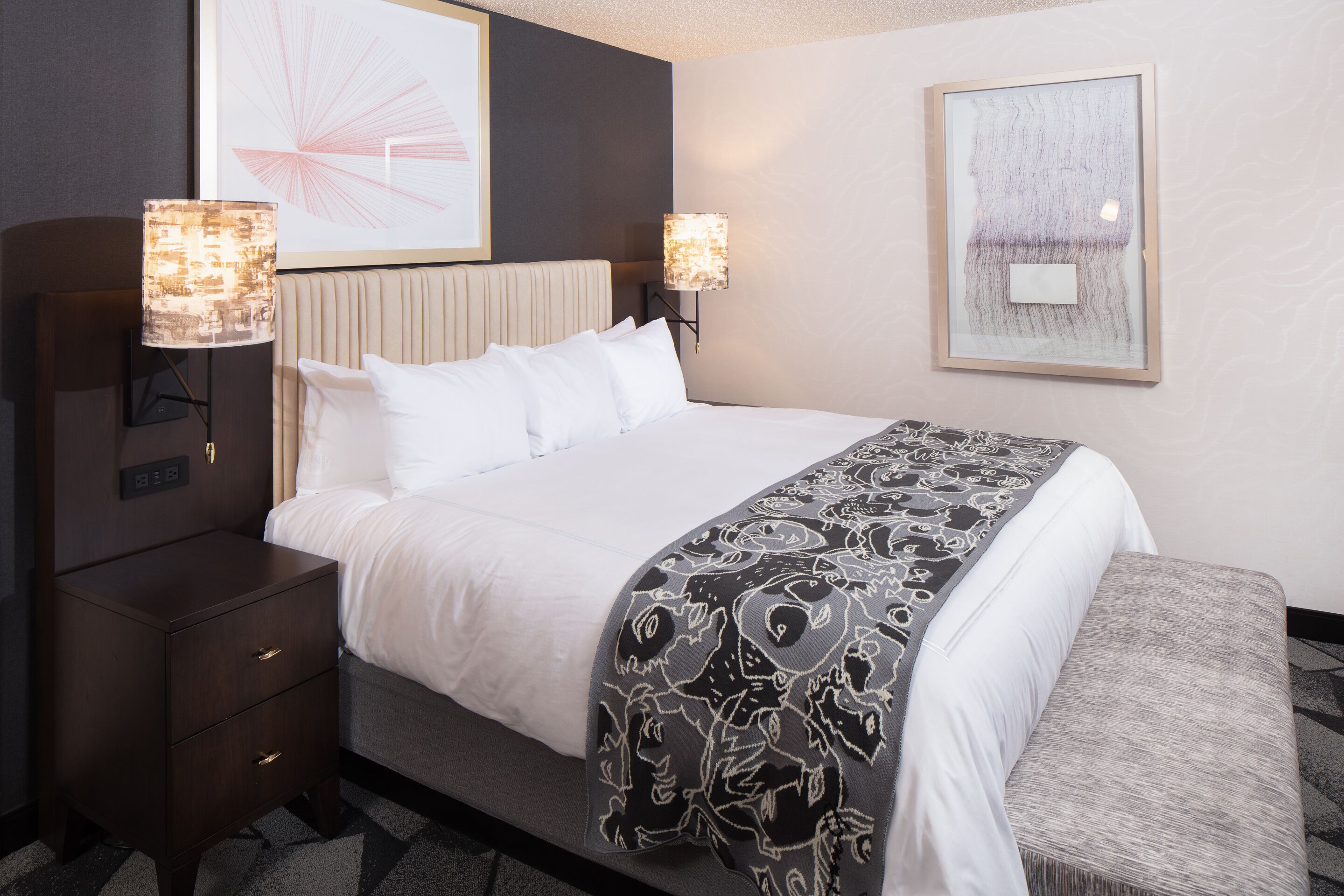 A hotel room with a bed, bedside tables, and wall-mounted lamps.