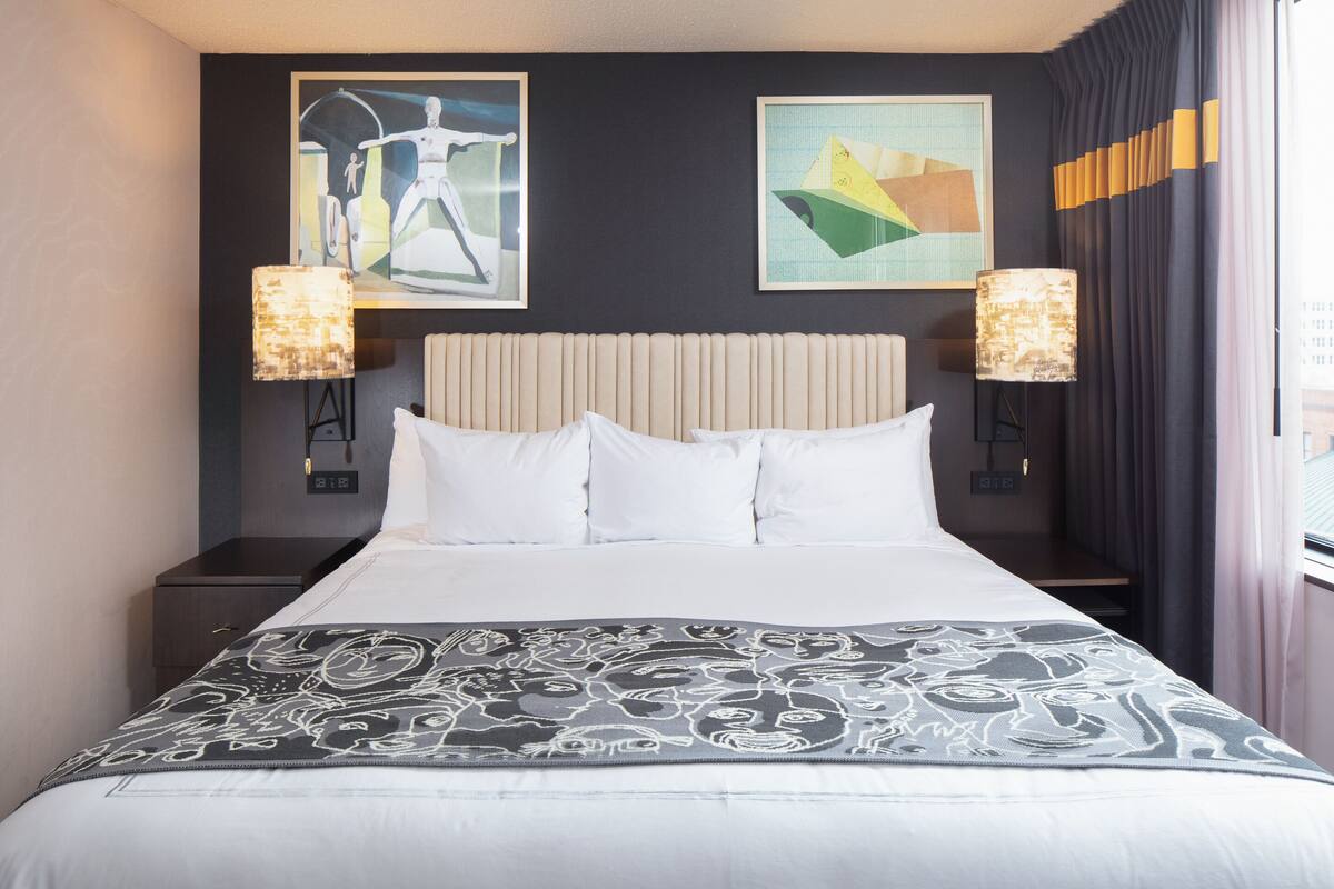 Une chambre d’hôtel avec un grand lit, deux tables de chevet, une petite table et deux lampes fixées au mur.