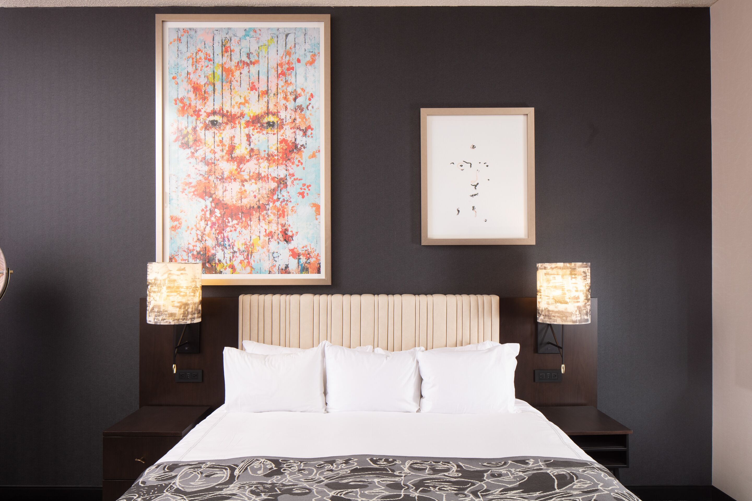 A hotel room with a large bed, two bedside tables, a nightstand, a headboard, and two wall-mounted lamps.