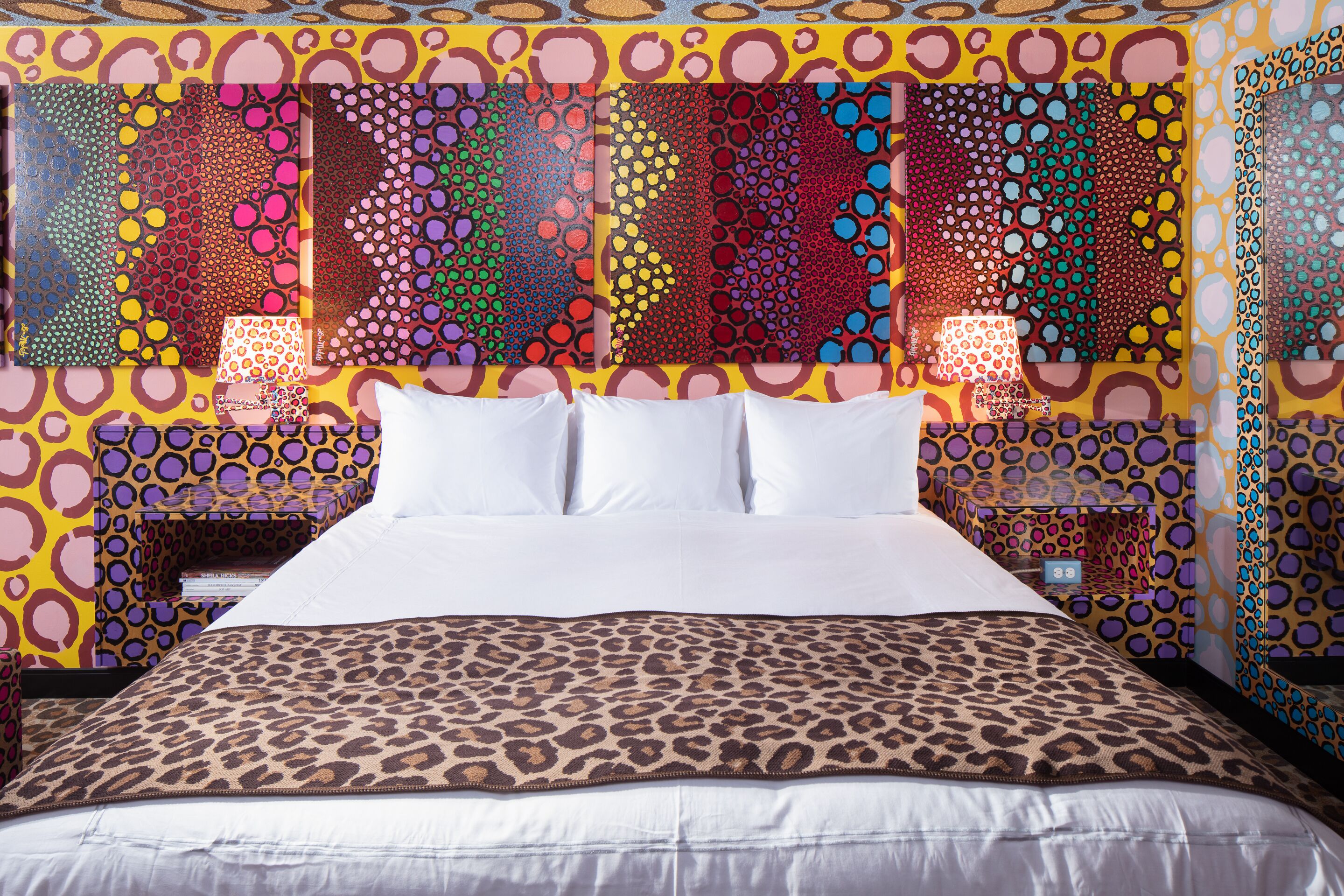 Una cama con colcha de estampado de leopardo, almohadas blancas y cabecera con un patrón abstracto y colorido.
