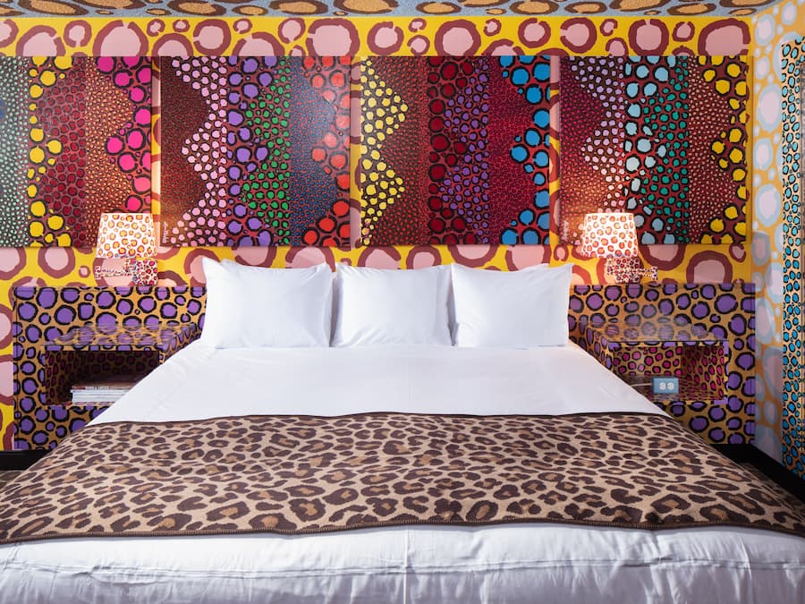 Una cama con colcha de estampado de leopardo, almohadas blancas y cabecera con un patrón abstracto y colorido.