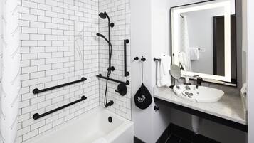 Un baño moderno con ducha de azulejos blancos, toallero negro, lavabo blanco con espejo y suelo negro.