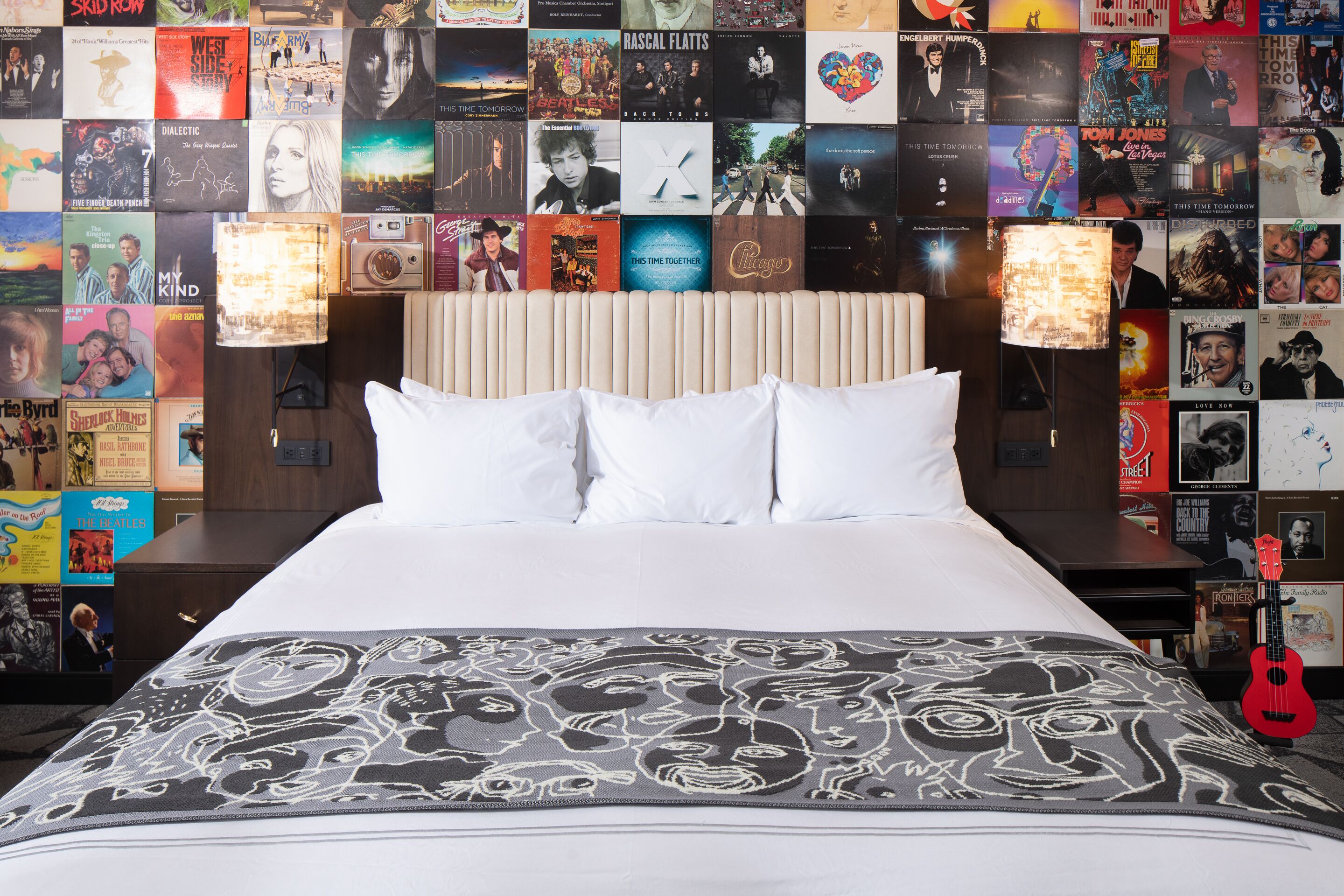 A hotel room with a large bed, a headboard with posters, and a guitar on the nightstand.