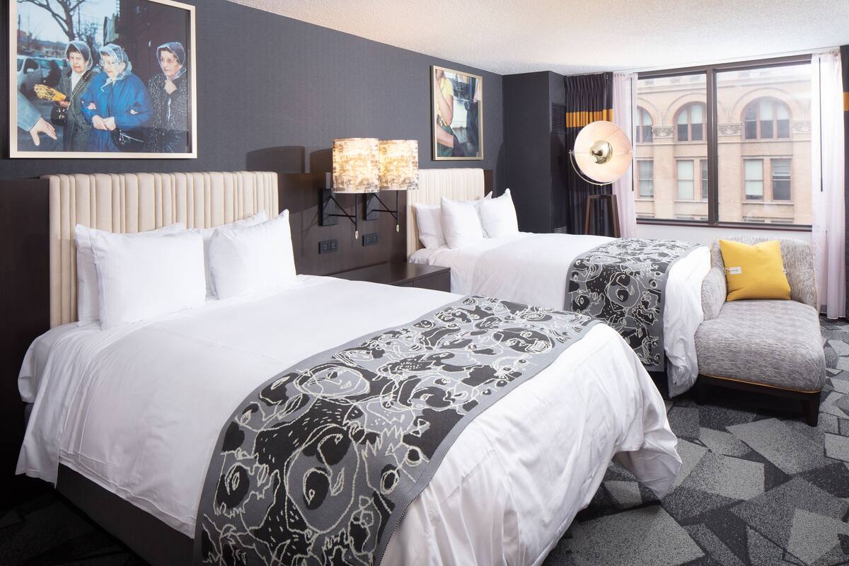 Une chambre d’hôtel avec deux lits, une table de chevet, une lampe et une vue sur la ville par la fenêtre.