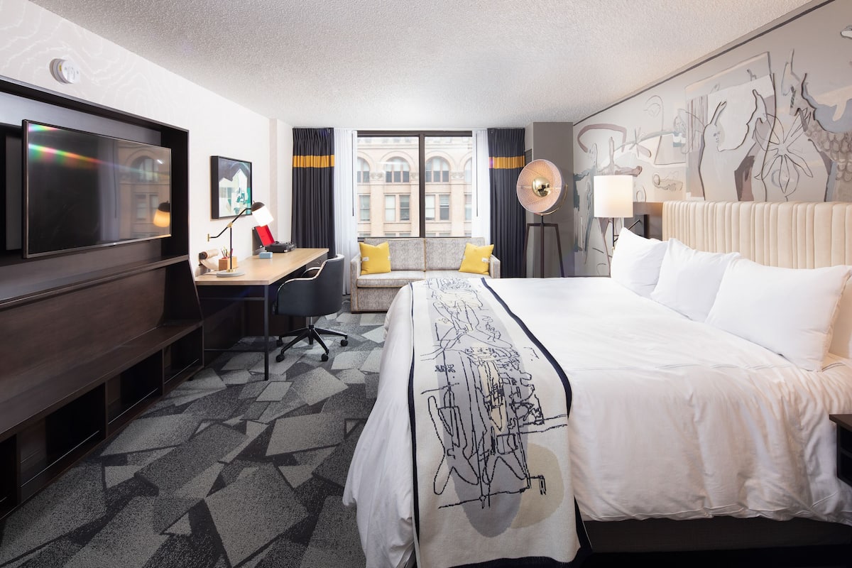 Une chambre d’hôtel avec un grand lit, un bureau avec une chaise, un téléviseur à écran plat et une fenêtre avec des rideaux.