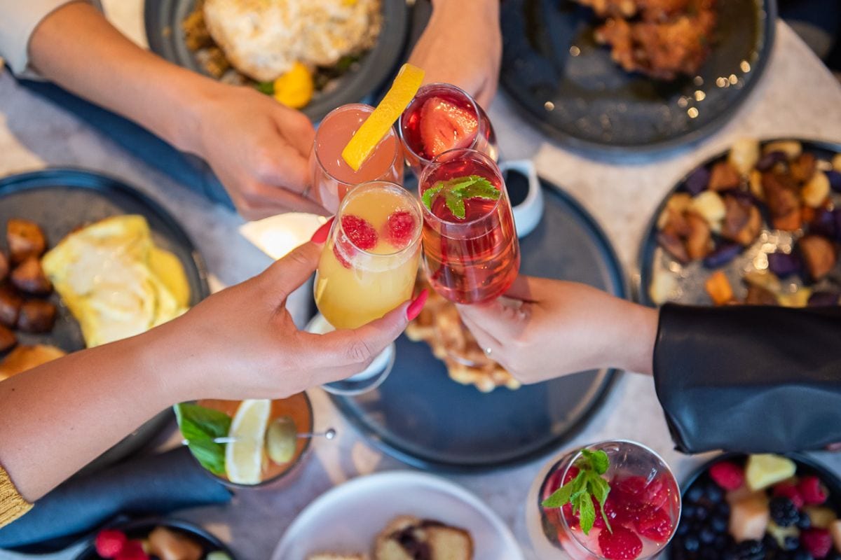 A group of people holding glasses with various beverages, surrounded by plates of food.