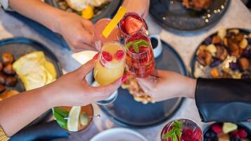 A group of people holding glasses with various beverages, surrounded by plates of food.
