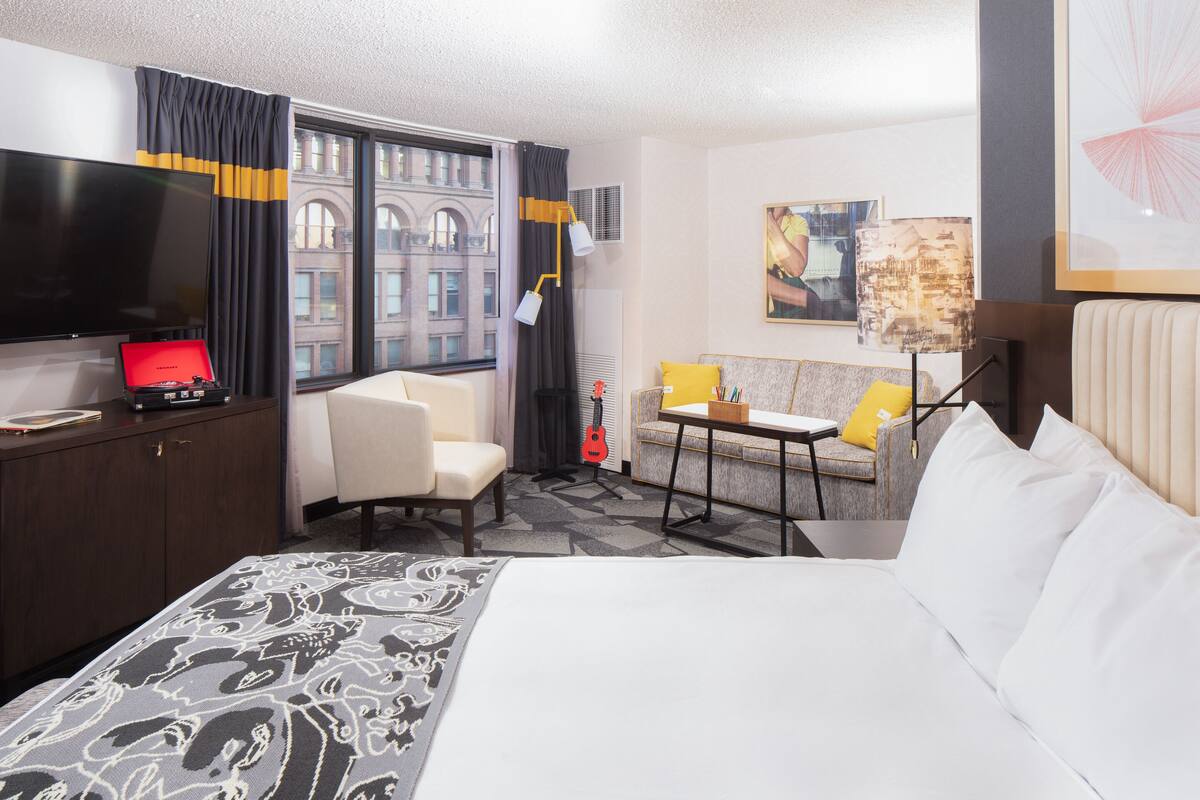 Une chambre d’hôtel avec un grand lit, une télévision, un bureau, une chaise et une vue sur le paysage urbain par la fenêtre.