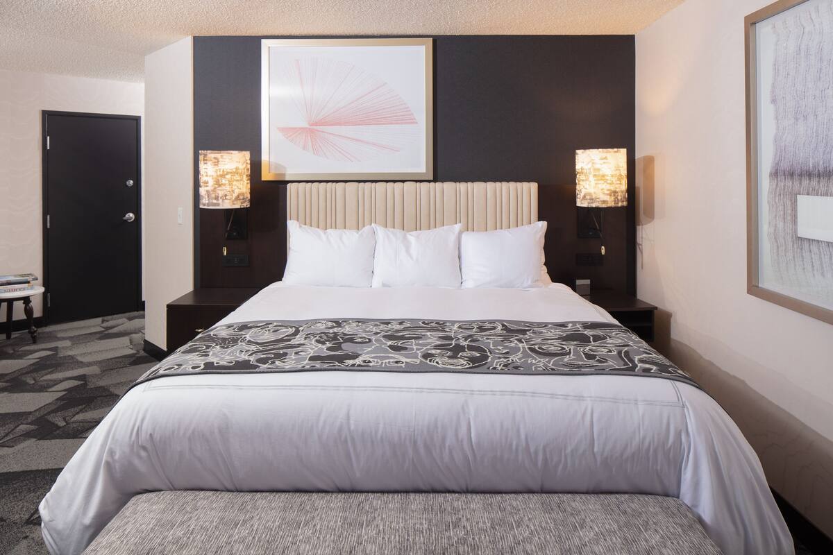 Une chambre d’hôtel avec un grand lit, deux tables de chevet et une tête de lit ornée d’un panneau décoratif.