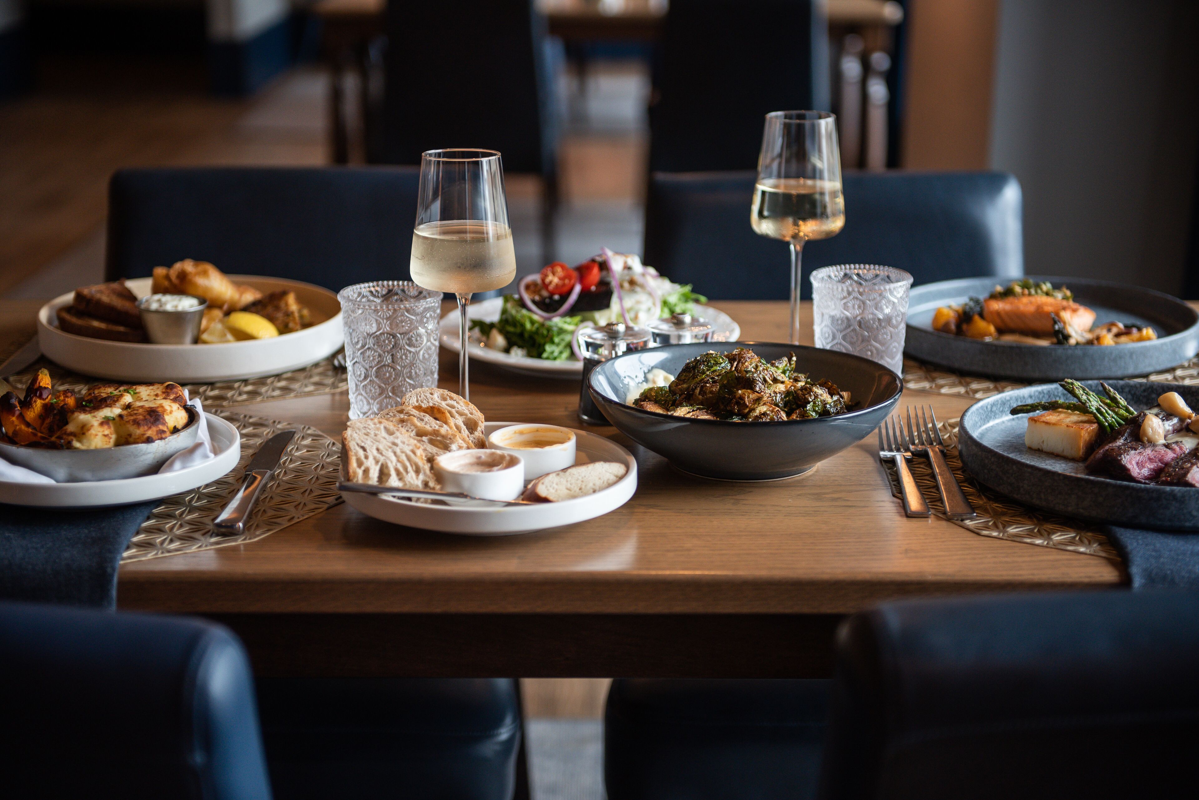 A dining table set with various dishes, glasses of wine, and cutlery.