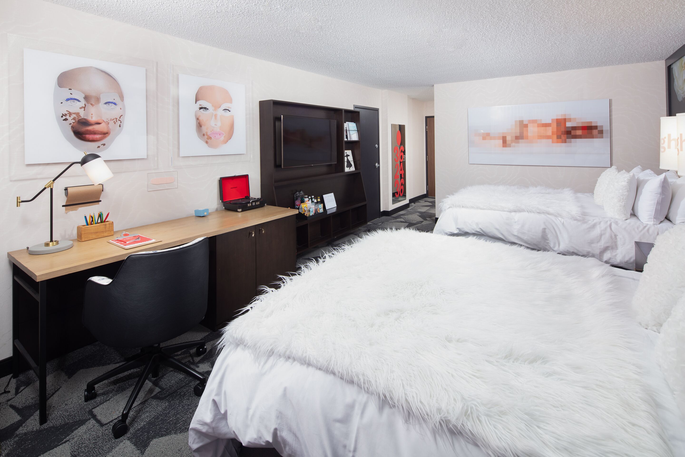 A hotel room with a large bed, a desk with a computer, a TV, and artwork on the walls.